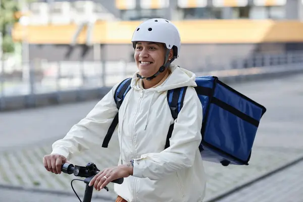 電動スクーターに乗っている間ヘルメットを身に着けている笑顔の食品配達労働者の肖像 — ストック写真