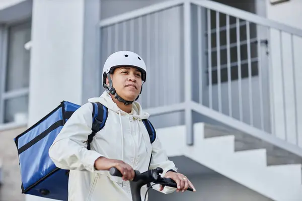 都市設定で電動スクーターに乗っている間にヘルメットを着用する食品配達労働者の最小ショット コピースペース — ストック写真