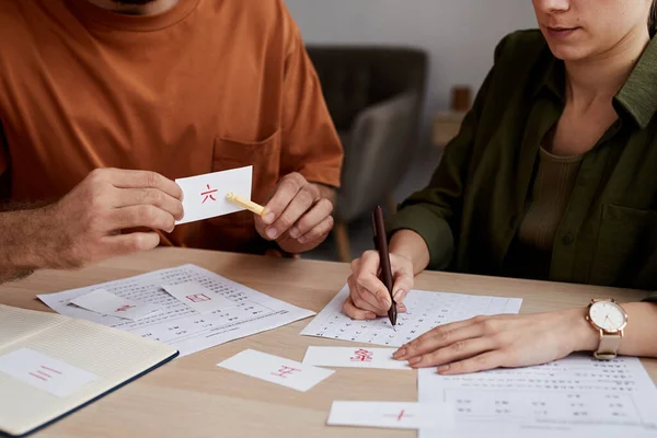 学生の前に座ってテストペーパーでそれを認識し チェックしながら ペーパーカードを指す中国語の男性のチューター — ストック写真