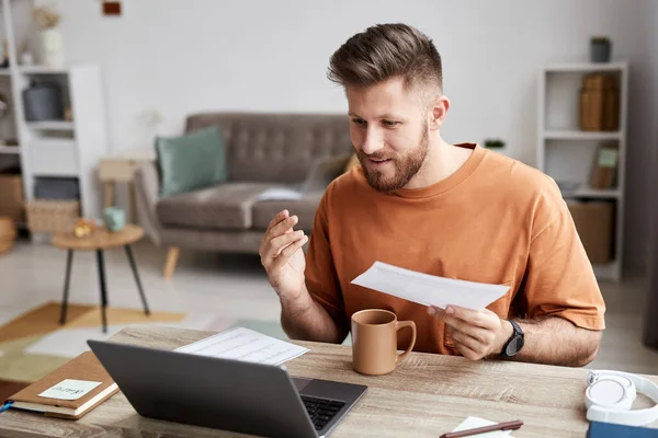 stock image Young confident businessman with paper communicating with his tutor in video chat during online lesson while sitting by desk in living room