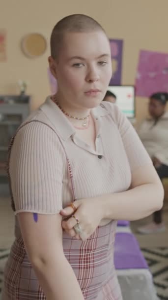 屋内に立っている彼女の肩に紫のフェミニストのシンボルを示す剃られた頭を持つ強力な若い白人女性の垂直中型のスローモの肖像画 — ストック動画