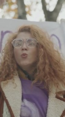 Açık hava gösteri toplantısında feminizm ideolojisi için mücadele ederken elini kaldıran ve sloganlar atan Kafkasyalı genç kadın protestocunun dikey yavaşlaması