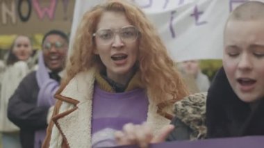Kadın hakları ve cinsiyet eşitliği için mücadele eden ellerinde posterler ve pankartlarla, grevde olan etnik çeşitliliğe sahip genç feminist kadınların kalabalığının belini kaldırın.