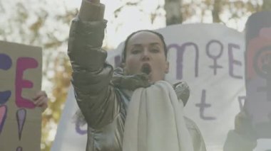 Protesto sırasında diğer kadınlarla birlikte yumruğunu kaldırıp feminist sloganlar atan duygusal, genç, beyaz bir kadın.
