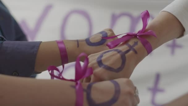 女性活動家の認識できない女性の拳のクローズアップ 手首に紫のリボンとフェミニストのシンボルが女性のエンパワーメントと平等を連帯してまとめられた — ストック動画