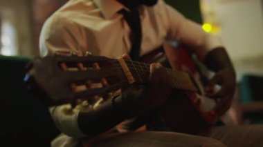 Caz kulübündeki konserden önce beyaz gömlek ve siyah kravat takıp akustik gitar ayarlayan tanınmamış caz gitaristinin yakın çekimi.