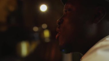 Siyah şapkalı genç siyahi erkek blues vokalistinin karanlık caz kulübünde loş ışıkla şarkı söylemesinin orta derecede yakın çekimi.