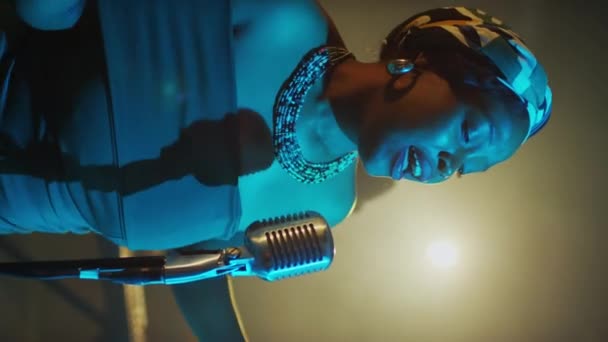 プロジェクターライトの下でブルースを歌う美しいアフリカ系アメリカ人女性音楽アーティストの垂直ミディアムショット ファンシーなジャズクラブでバンドとのライブコンサート — ストック動画