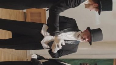 Smokinli, silindir şapkalı ve eldivenli üç farklı adamın balo salonunda daireler çizip balo partisinin başlamasını beklerken sohbet ettikleri dikey bir kare.