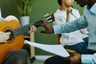 Müzik öğretmeninin ve öğrencinin elleri akustik gitarın tellerine dokunurken liseli kız da bunu derste çalmayı öğreniyor.