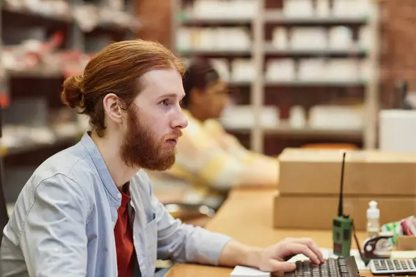Side view portrait of bearded young man using computer at printing shop or publishing company, copy space