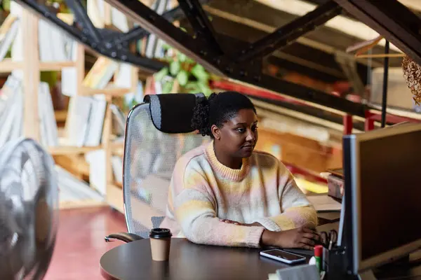 Portrait of young black woman using computer at workplace in printing shop or publishing company, copy space