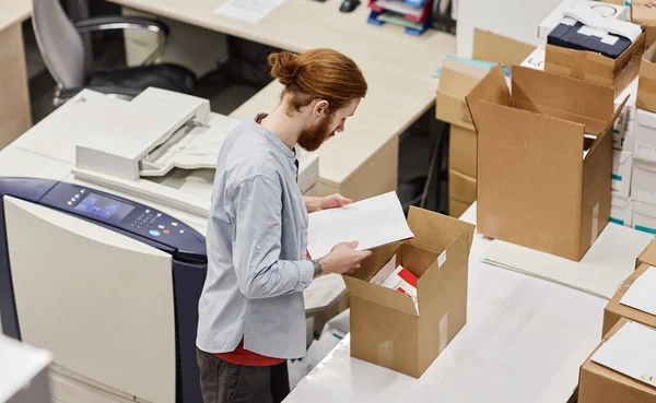High angle portrait of young man packaging print products in publishing shop, copy space