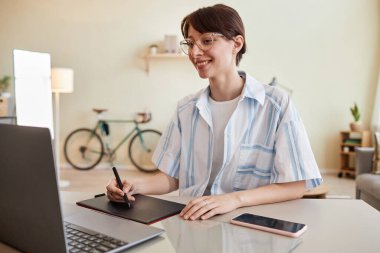 Dijital tasarım veya fotoğraf düzenleme için ofis işyerinde kalem tableti kullanan gülümseyen genç bir kadının portresi