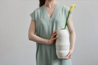 Elinde çiçekli el yapımı seramik vazo tutan tanınmayan genç bir kadının minimal yakın çekimi.