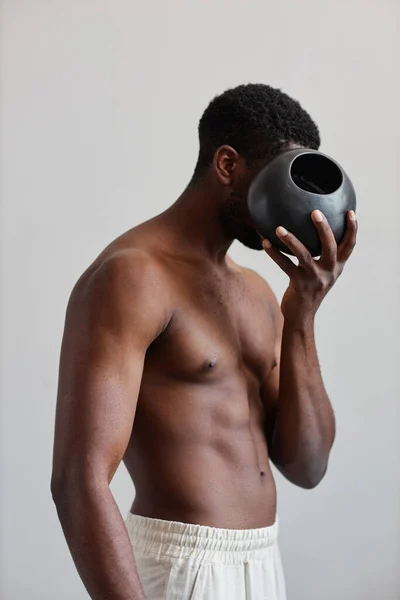 タンセラミック花瓶を保持し 顔を隠すシャツレス黒人の最小限のコンセプトの肖像画 デザインの自然な形 — ストック写真