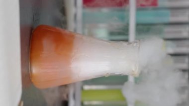 Dikey olarak, kimya laboratuarında yapılan deney sırasında hiç kimse tanınmayan turuncu sıvının cam şişede fokurdamasına ve buharlaşmasına yaklaşamaz.