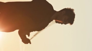 Altın gün batımında yanan ateş zincirleriyle hokkabazlık yapan profesyonel ateş gösterisi sanatçısının dikey orta pozu