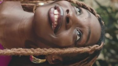 Mor elbiseli çekici Afrikalı nedimenin dikey portresi güzel düğün salonundaki tropik bitkiler arasında kamera önünde poz veriyor.