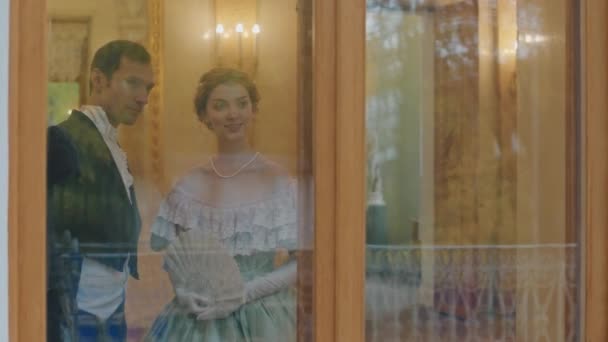 白种人年轻夫妇穿着摄政风格的衣服 透过窗户慢慢地看过去 一边看着窗户 一边聊天 一边一起参加新婚舞会 — 图库视频影像