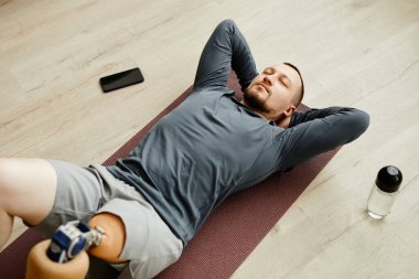 Protez bacaklı bir adamın evde yoga minderiyle egzersiz yapması.