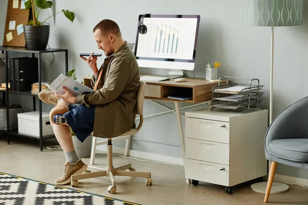 Side view portrait of man with prosthetic leg reading document at workplace in office and recording voice message, copy space