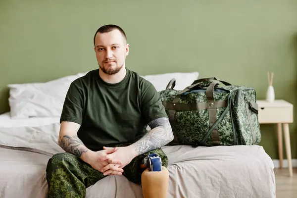 Portrait of military veteran with prosthetic leg looking at camera at home and wearing army uniform, copy space