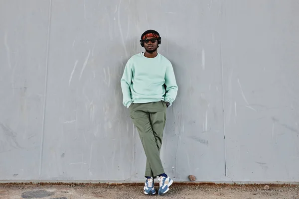 Minimal full length portrait of young black man wearing street style clothes leaning on concrete wall outdoors, copy space