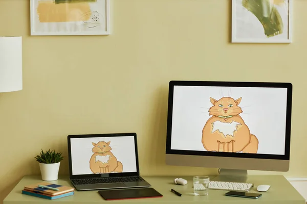 Workplace of modern digital artist or freelancer with laptop and desktop computer monitor with drawn picture of fluffy red cat