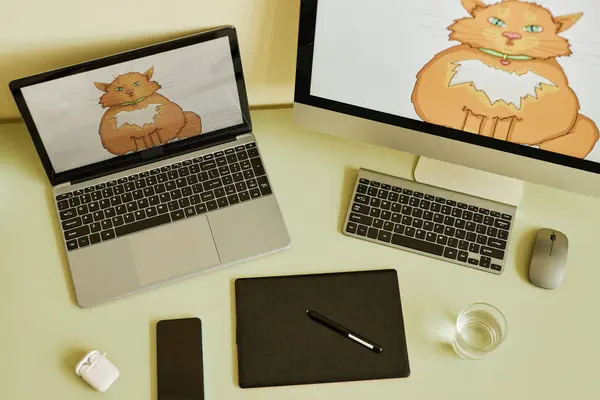 Above view of laptop and computer with fat red cat on screens on workplace of digital artist with mobile gadgets and desktop devices