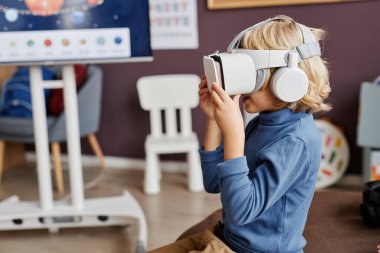 Anaokulunda kameranın önünde otururken sarışın şirin çocuğun sanal oyun oynamasının yan görüntüsü.