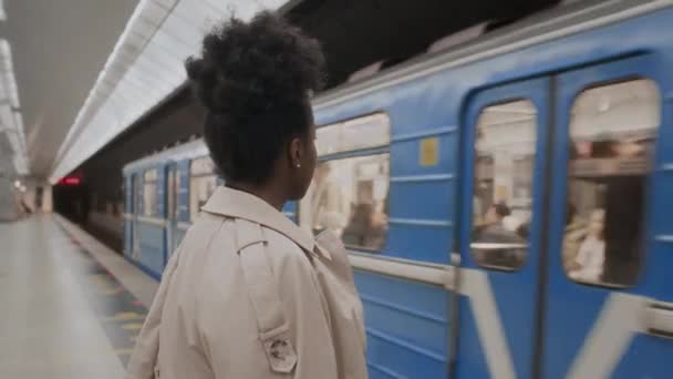 让年轻的黑人妇女站在地铁站的月台上 靠着从后面经过的火车站起来 — 图库视频影像