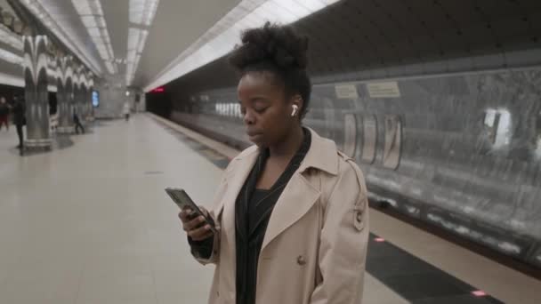 Medium Shot Van Jonge Zwarte Vrouw Draadloze Oortelefoons Staan Metrostation — Stockvideo