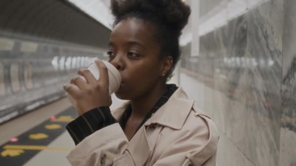年轻的黑人女商人在地铁站等地铁的时候 一边用一次性杯子喝着咖啡 一边用智能手机发短信 — 图库视频影像