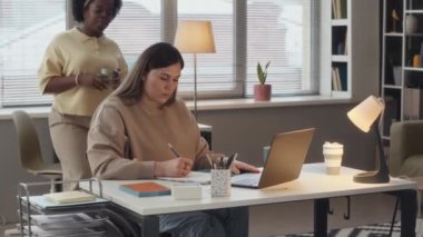 Modern ofiste birlikte çalışan iki genç kadının laptopta sunumu tartıştıkları ve fikirleri paylaştığı orta boy bir fotoğraf.