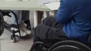Tekerlekli sandalyedeki ofis çalışanlarından oluşan yavaş yavaş oluşan yaratıcı ekip modern ofislerinde toplantı yapıyor.