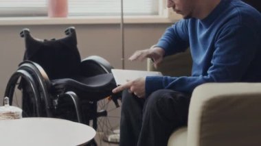 Kafkasyalı engelli bir adamın rahat bir çalışma alanında kanepe üzerinde çalışırken dizüstü bilgisayar kullanmasının yan görüntüsü.
