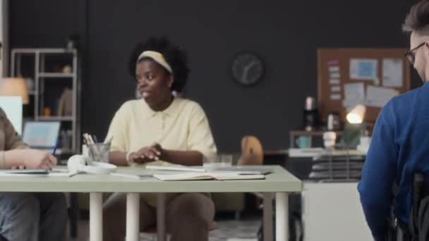 中镜头 年轻的白人残疾男子坐轮椅向办公室 与两名多族裔女性同事一起参加头脑风暴会议 — 图库视频影像