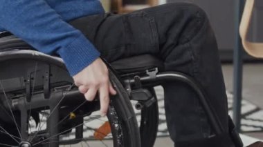 Tekerlekli sandalyedeki tanınmayan adamın, masa başında boş yer açmak için ahşap ofis sandalyesini hareket ettirmesi ve işe başlaması.