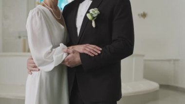 Beyaz kilisenin beyaz camlı camına karşı kameraya poz veren son sınıf beyaz evli çiftin orta boy portresi.