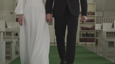 Beyaz, orta yaşlı, zarif düğün kostümleri giyen, yeşil halıda yürüyen, mihrabın önündeki sıralar arasında yürüyen, kilisede güzel bir düğün töreni yapan çift yavaşlıyor.