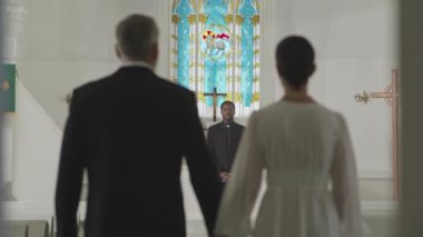 Beyaz tenli olgun damat ve gelinin yavaş yavaş siyah erkek papaza doğru yürümesi güzel bir kilise nikahı sırasında