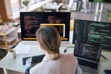 Kadın geliştirici bilgisayardaki programlama kodunu kontrol ediyor, arkadan görüntüle