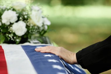 Erkek eli tabutun üzerinde, Amerikan bayrağıyla kaplanmış bir şekilde açık hava cenaze töreninde elveda diyor.