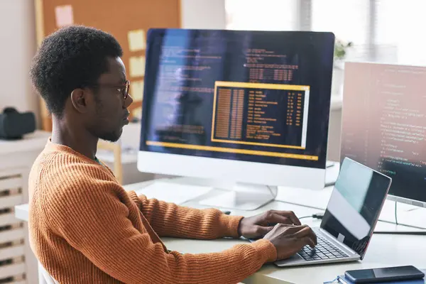 Serious young Black man in warm orange sweater concentrated on coding