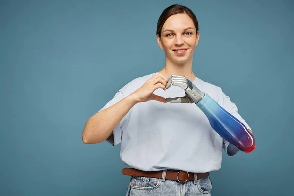 Portrait of smiling woman with bionic hand making heart gesture