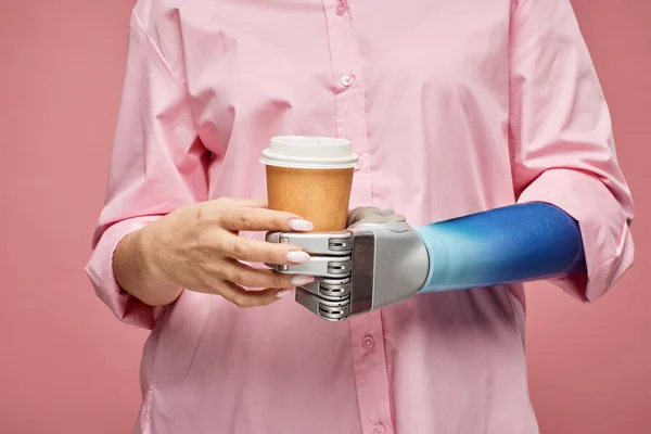 Closeup image of woman with bionic arm holding cup of take-out coffee
