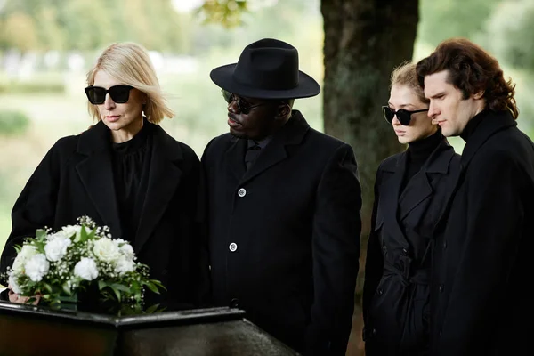 サングラスで黒を着て コピースペースで屋外の葬儀で棺で立っている人々のグループ — ストック写真