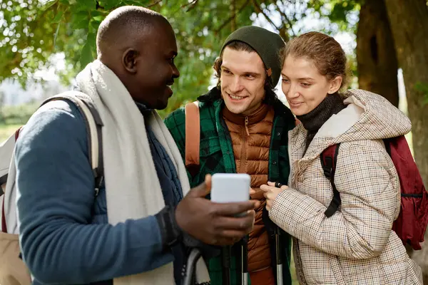 Diverse group of three people looking at smartphone screen while hiking outdoors
