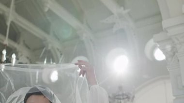 Beyaz duvak takan beyaz bir kadın ve düğün günü kilisede kameraya poz veren inci kolyeli zarif bir gelinlik.